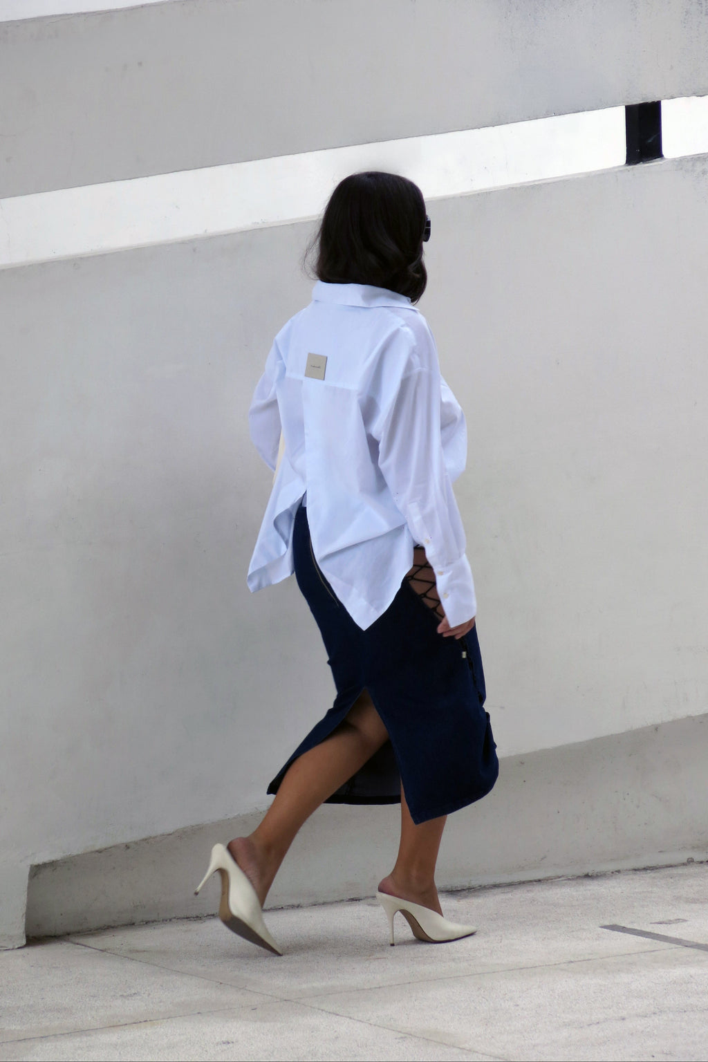 Modelo usando Saia Jeans Midi Amarrações Azul Karoline Vitto e Camisa Split Costas, vista traseira